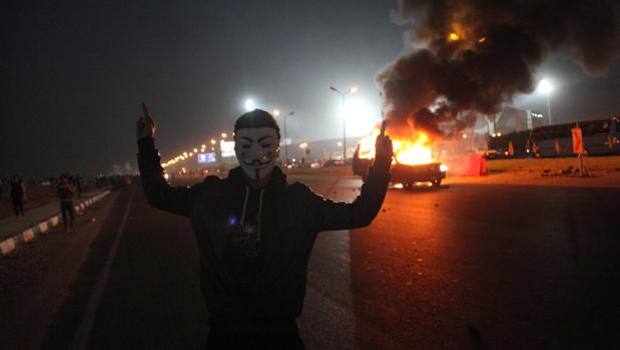 Un ultra egiziano con la maschera di Anonymous. Dietro, l'inferno. Afp